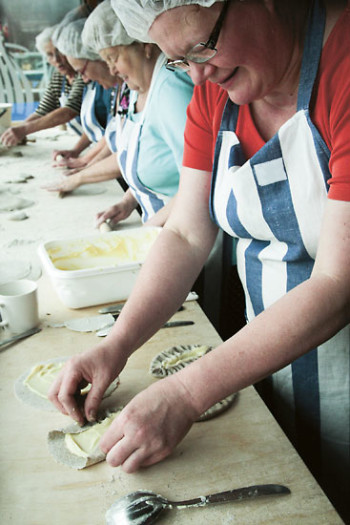 Elderly women in a row by a table making Karelian pasties.