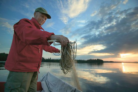 A man standing by a lake untangling a fishing line.
