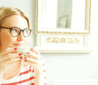 A woman sitting with a coffee cup in hand, staring thoughtfully into the distance.