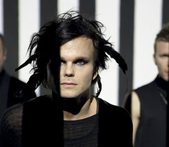 Lauri from The Rasmus with his signature black hair with feathers and dark eye makeup; the other band members in the background.