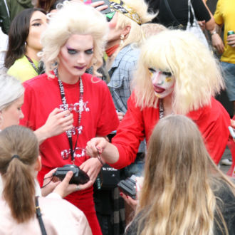 Performers in red drag outfits talk with fans.