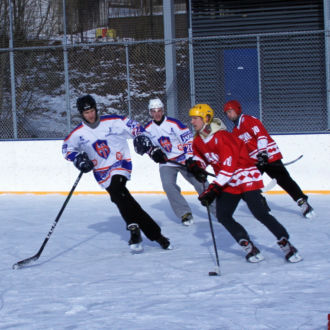 Cinco jogadores de hóquei no gelo patinam atrás do disco em uma pista de gelo ao ar livre