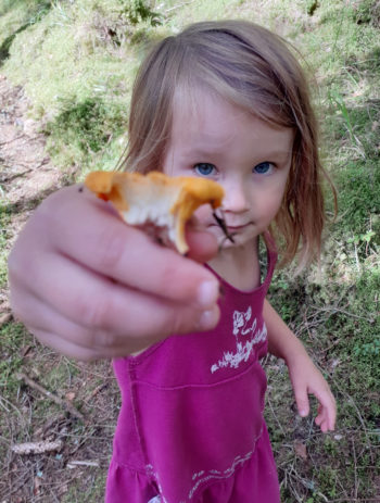 Uma garota segura um cogumelo que colheu na floresta.