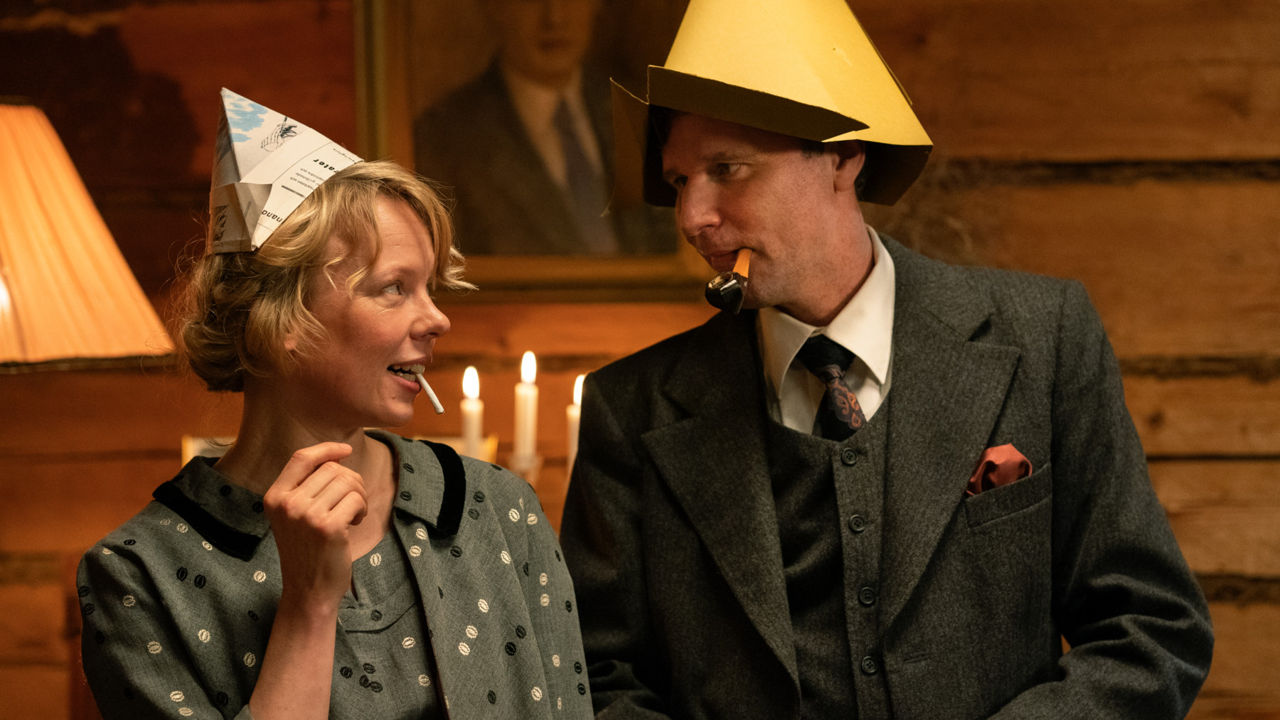 A woman and a man wearing pointed party hats look at each other.