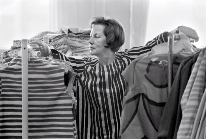 A woman in a striped blouse stands between two racks of similarly striped clothing.