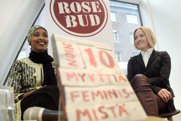 Two women are visible, one on each side of a book that is on a table very close to the camera.