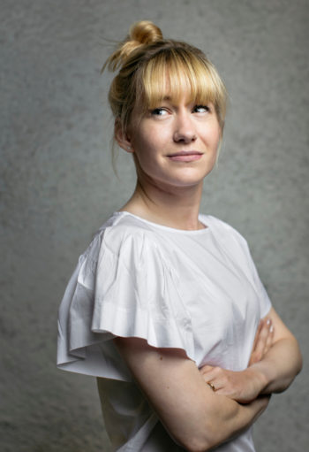 A woman with her arms crossed over her chest looks past the camera at something outside the frame.