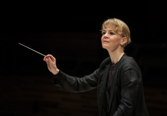 A woman with a conductor’s baton is leading an orchestra that is not shown in the photo.