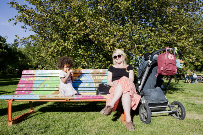A mother and child sit on a park bench in the sun.