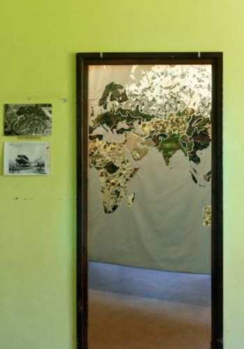 En una pared hay un mapa del mundo enmarcado, hecho de retazos de tela de camuflaje.