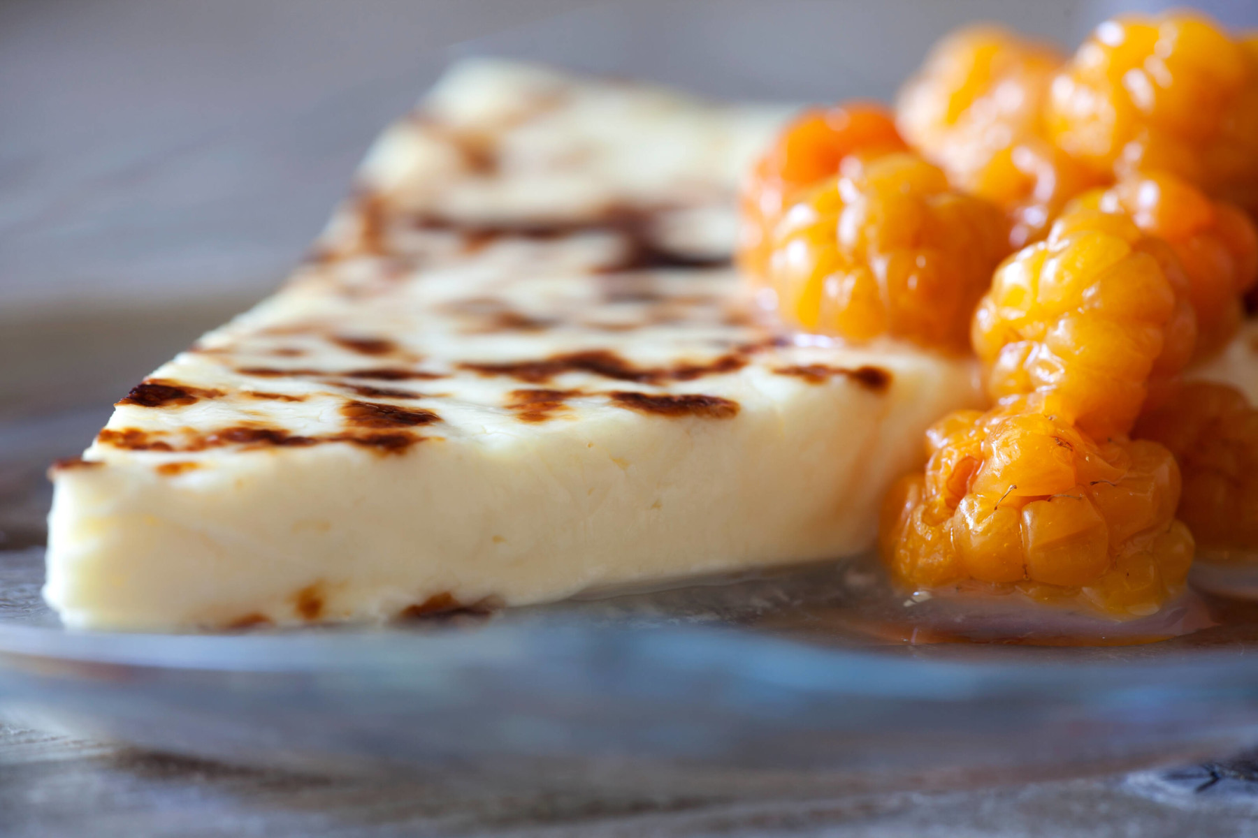 Um pedaço de queijo num prato com grandes amoras cor de laranja.