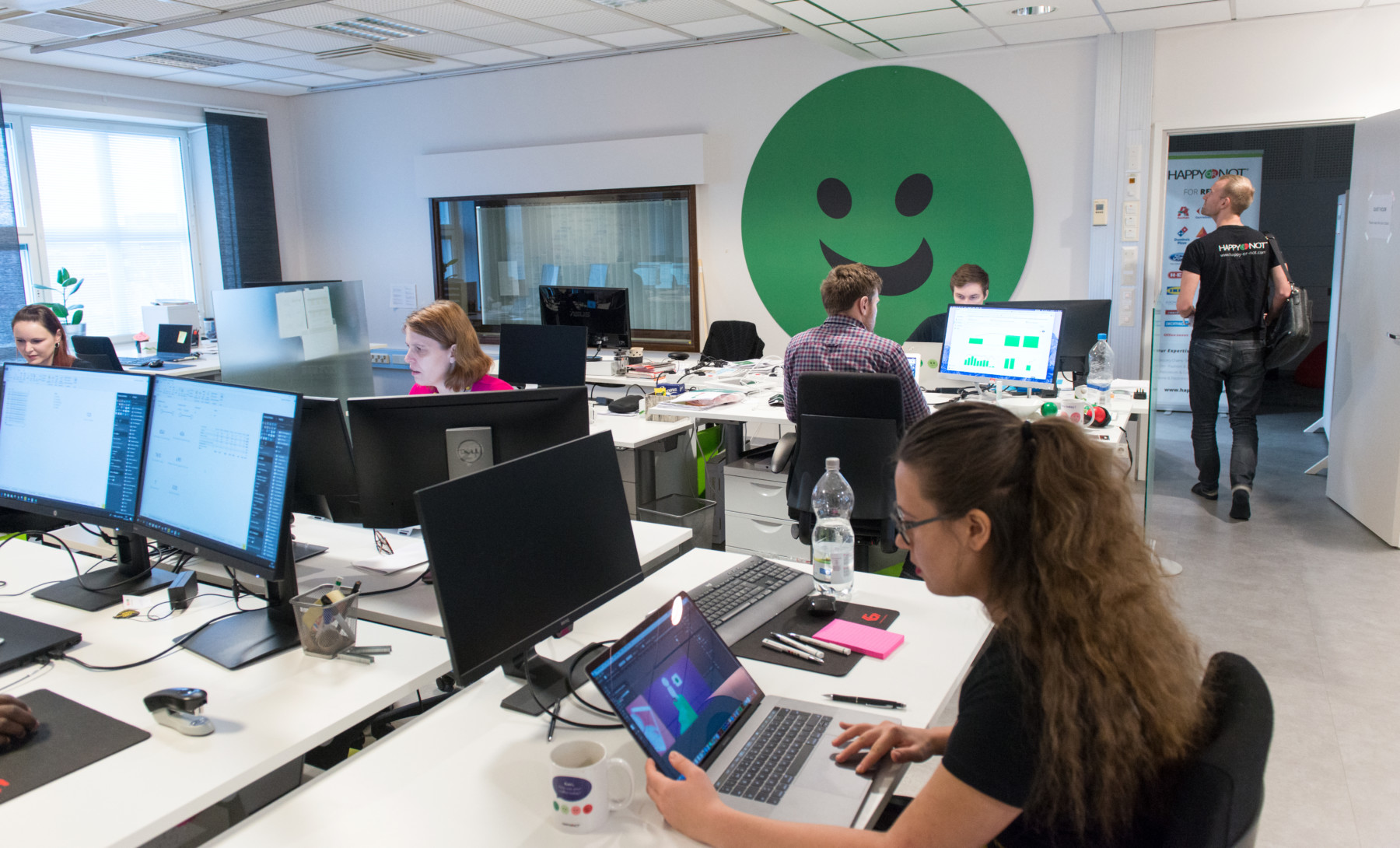 Several women and men sit at their computers in a bright modern office.
