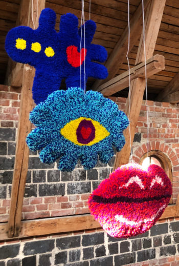 Artworks depicting a pair of lips, an eye and an airplane hang in an exhibition space.
