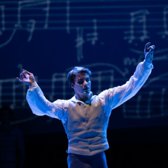 A man stands with his hands outstretched in front of a picture of music notes.