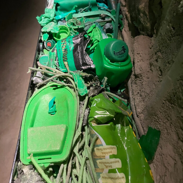 Pieces of plastic trash, all green, including a toy boat, candy wrappers and a bottle top.