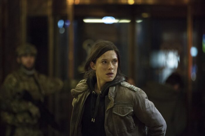 A woman wearing a military jacket watches something outside the frame of the photo, with a stressed look on her face.