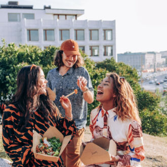 With a view of Helsinki in the background, three women and a man are laughing and enjoying a picnic in a park.