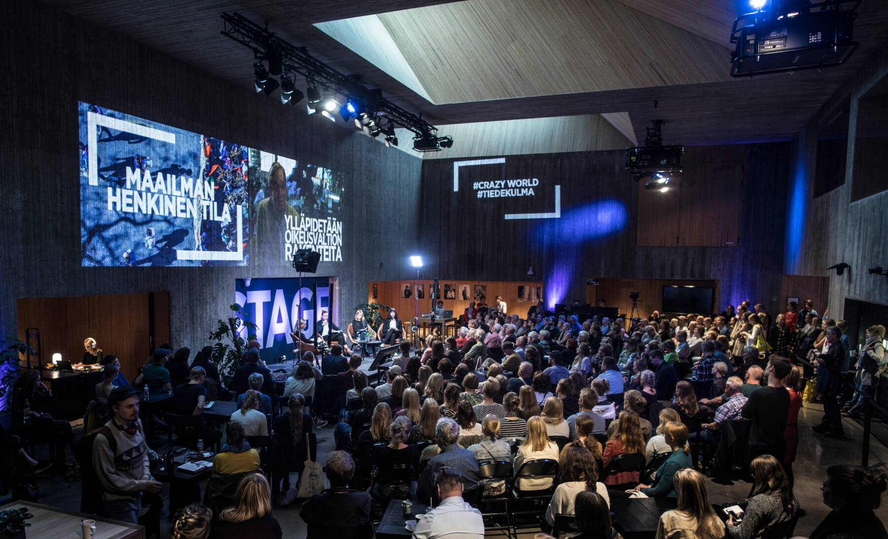 An audience is seated in a large space listening to several people who are having a discussion on a stage.