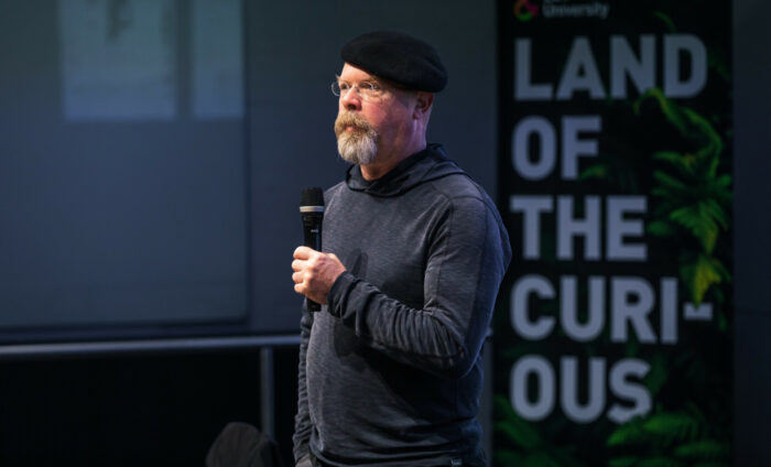 A man wearing a beret and a grey goatee talks into a microphone.